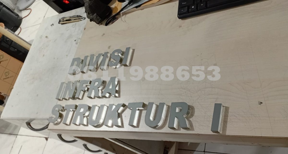 Huruf timbul akrilik custom tulisan DIVISI INFRASTRUKTUR untuk signage kantor dan papan nama gedung modern.